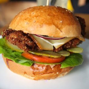 Delicious crispy chicken burger with fresh veggies and cheese on a sesame seed bun, served on a plate.